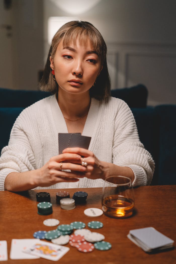 An Asian woman playing poker at home, focused and serious, showcasing a strategic mindset.